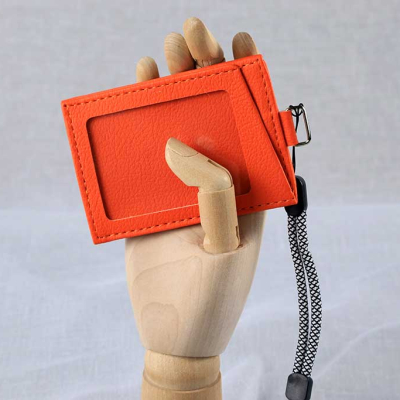 Оранжев кожен кардхолдер/бадж за лични карти, държан от дървен манекен на ръка.