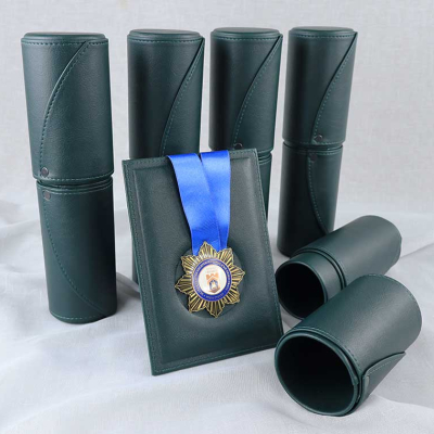 Златист медал със синя лента в тъмнозелена кожена рамка и комплект от съпътстващи кожени тубуси.